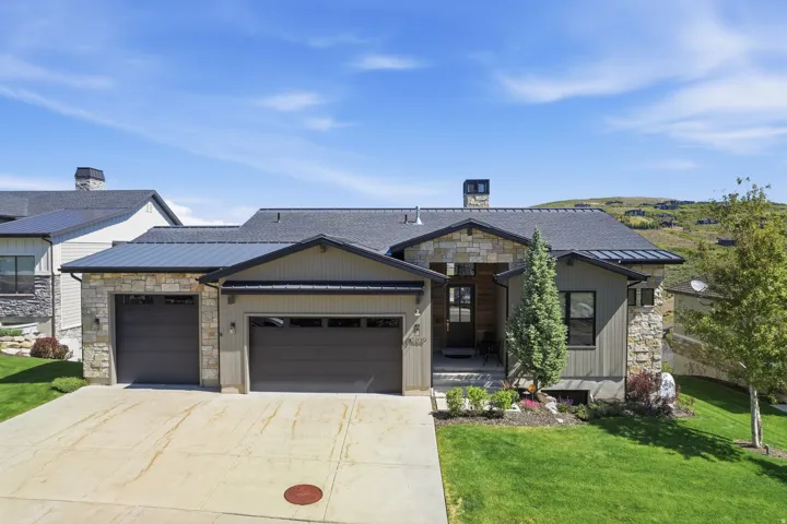 Modern residence featuring a stone and siding exterior, a two-car garage, a metal accent roof, and a concrete driveway