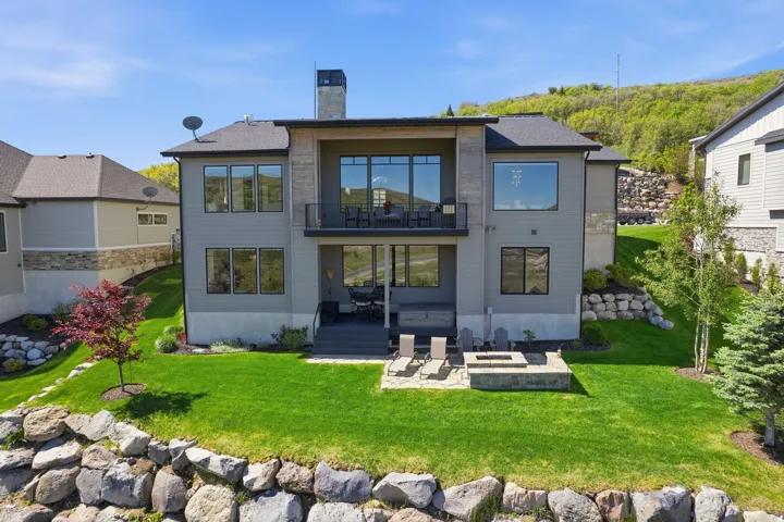 Rear exterior featuring a stone fire pit, lower patio with built-in hot tub, upper balcony, and a manicured lawn