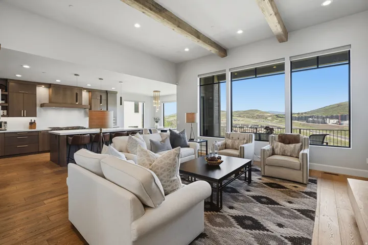 Open-concept living space featuring high ceilings with exposed wood beams, expansive windows, wood-finish flooring, a contemporary kitchen with an island, and a balcony with metal railings