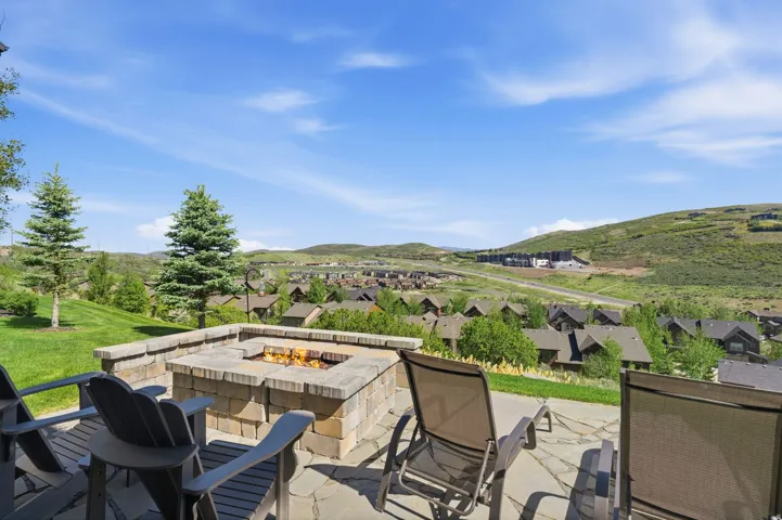 Stone paver patio featuring a built-in fire pit, stone block retaining wall, and expansive green lawn