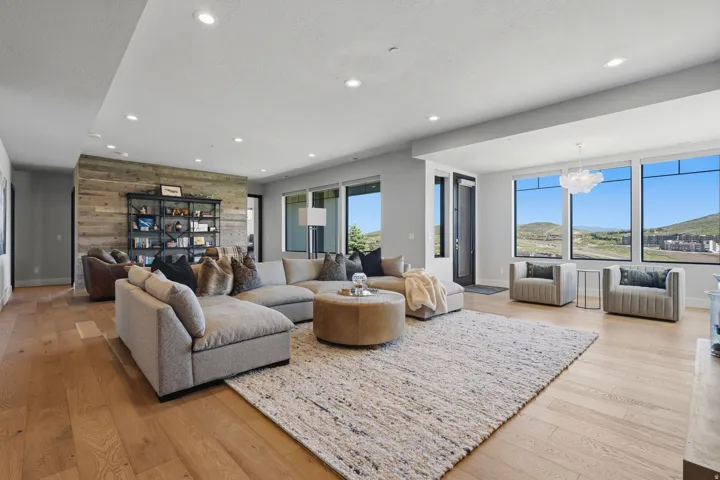 Spacious living area featuring light wood-finish flooring, a textured area rug, and a prominent wood-paneled accent wall