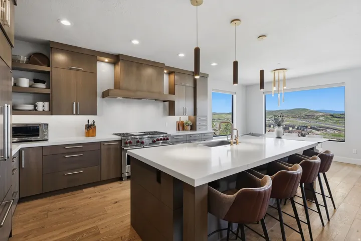 Expansive kitchen featuring a large central island with seating, stainless steel appliances, wood-finish flooring, custom cabinetry, and significant natural light through large windows