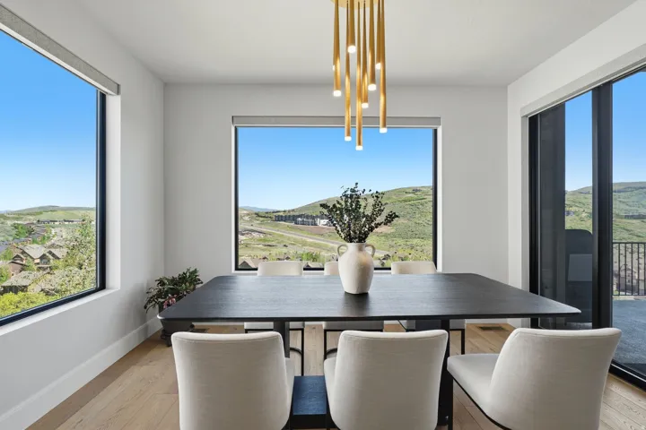 Open-concept dining area featuring a modern chandelier, light wood-finish flooring, and expansive windows showcasing a distant mountainous landscape