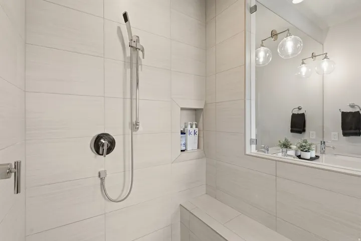 Shower enclosure featuring light-toned rectangular wall tiles, a built-in showering bench, and a recessed storage niche
