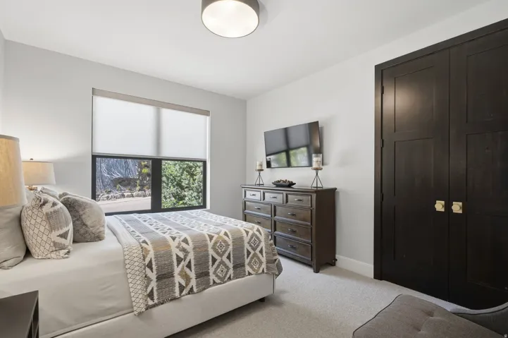 Bedroom featuring a window with roller shades, light gray wall paint, and dark wood-finish bi-fold closet doors with brass hardware