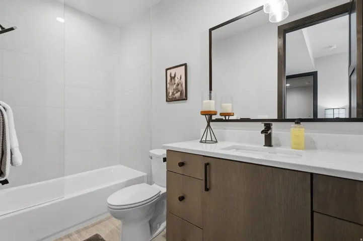 Modern bathroom featuring a wood-finish vanity with ample storage, a white countertop with integrated sink, and a large framed mirror
