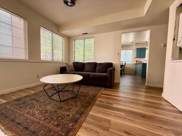 Living area featuring wood-finish flooring, ample natural light from multiple windows, crown molding, and a semi-open doorway to the kitchen