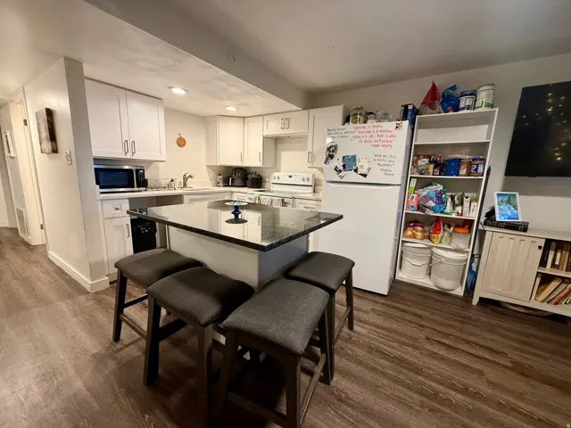 Kitchen featuring an island with seating, white cabinetry, light countertops, and wood-finish flooring