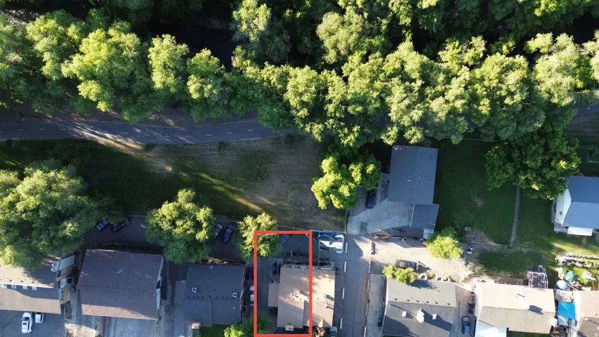 Aerial view showcasing the property outlined in orange, featuring a dark-toned roof and a prominent surrounding tree canopy