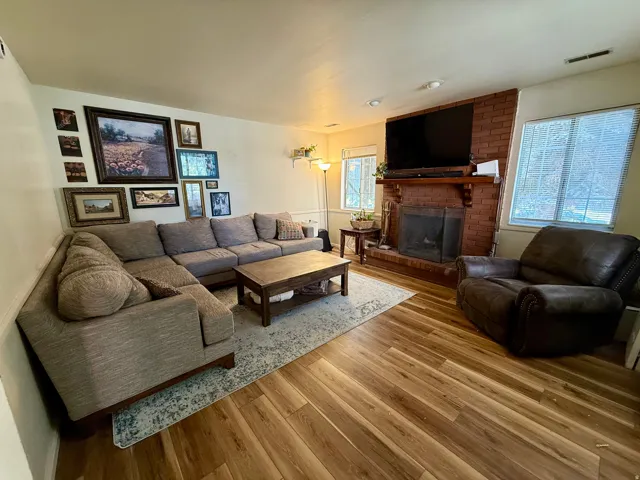 Living area featuring wood-finish flooring, a brick fireplace with a wood mantel, and multiple windows