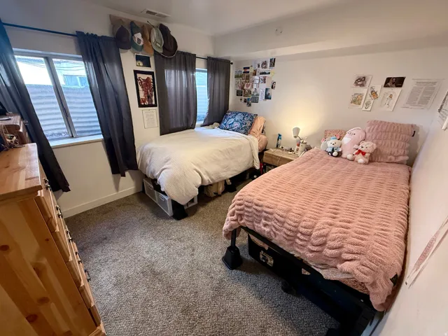 Carpeted room with white walls, two windows featuring dark curtains, and a light wood-finish dresser with dark hardware
