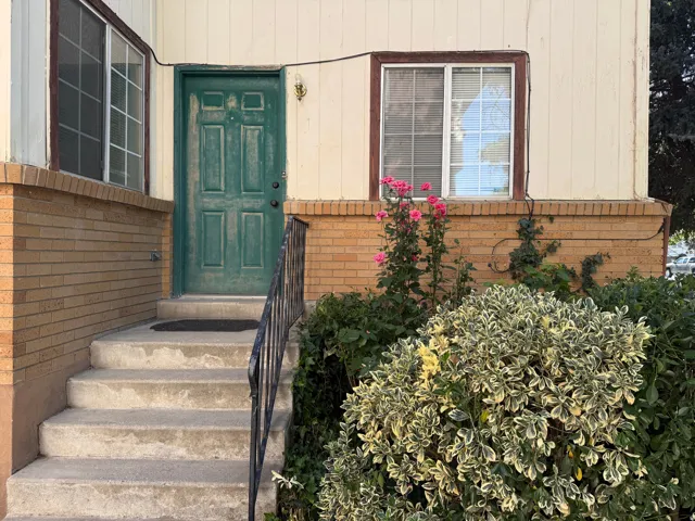 Entryway featuring concrete steps with a black metal handrail, a green paneled door, and a light-colored brick foundation
