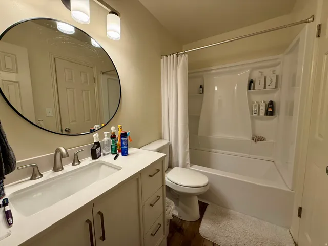 Bathroom featuring an integrated sink with a light-toned countertop, a matching vanity with cabinet and drawer storage, brushed nickel fixtures, a circular mirror, and a white tub/shower combination