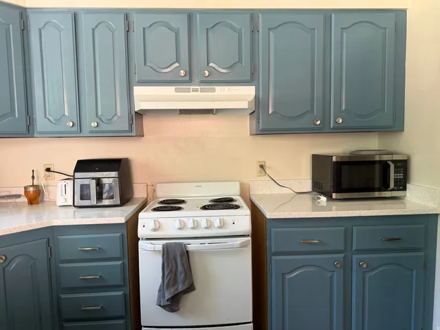 Kitchen featuring blue cabinetry with silver-tone hardware, white countertops, and a white electric range with an overhead vent hood