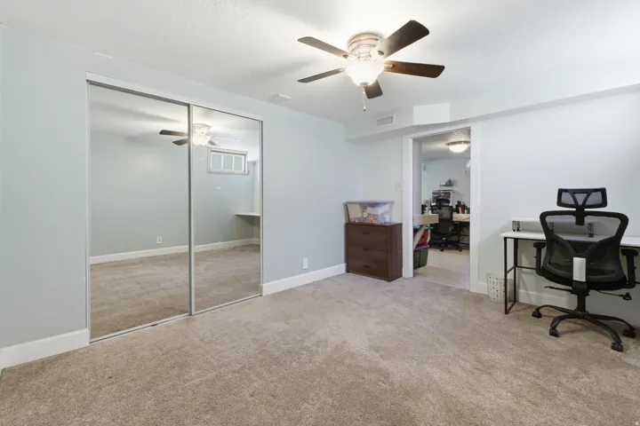 Carpeted room featuring mirrored sliding closet doors and a ceiling fan with integrated lighting