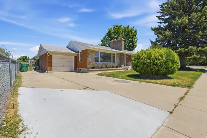 Brick and stone exterior featuring an attached garage, a chimney, and a concrete driveway