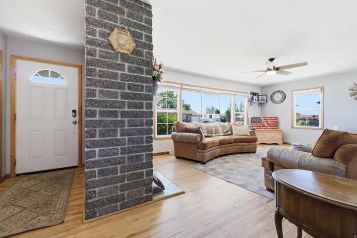 Spacious living area featuring wood-finish flooring, a ceiling fan, and large windows providing abundant natural light