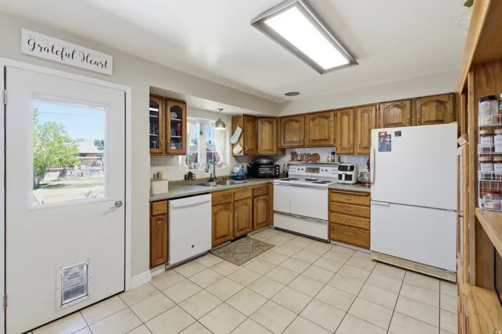 Kitchen featuring wood cabinetry, white appliances, and light-toned tile flooring