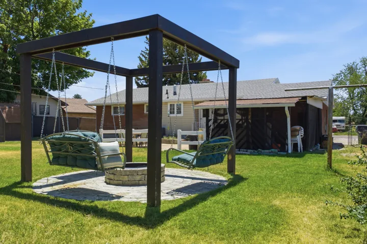 Backyard entertainment area featuring a dark-toned pergola, two suspended swings, a stone fire pit, and a paver patio
