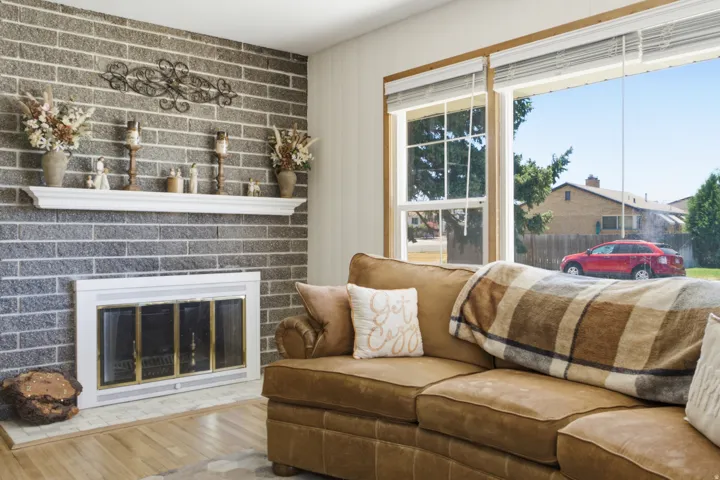 Wood-finish flooring with a brick-style accent wall and fireplace featuring a white mantel