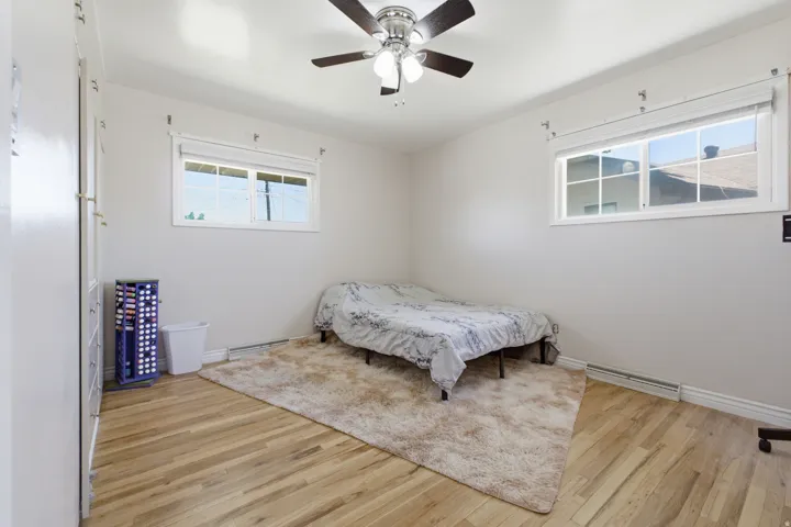 Light-filled room featuring wood-finish flooring, two windows with white blinds, a ceiling fan with integrated lighting, and white walls