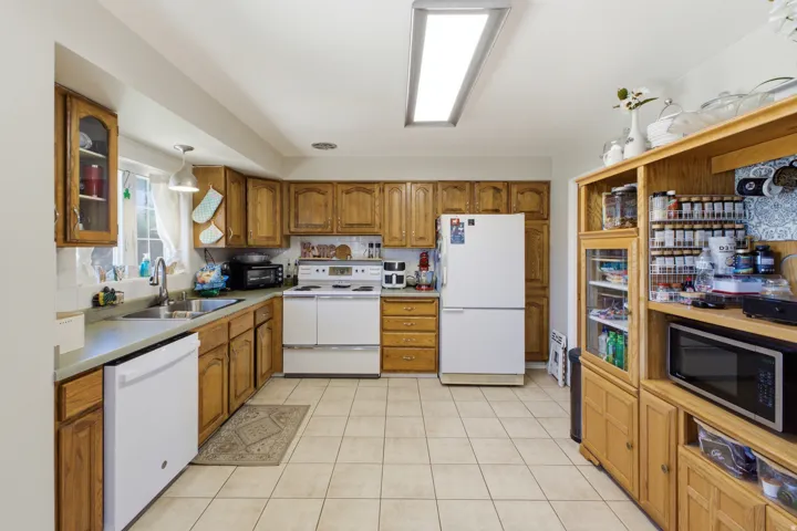 Kitchen featuring wood cabinetry, light-toned countertops, white appliances, and tiled flooring