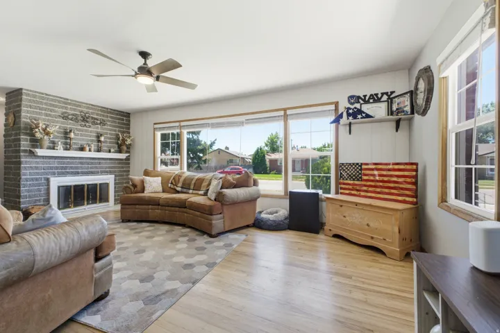 Spacious living area featuring light wood-finish flooring, a contemporary ceiling fan, and a prominent gray brick fireplace with a white mantel