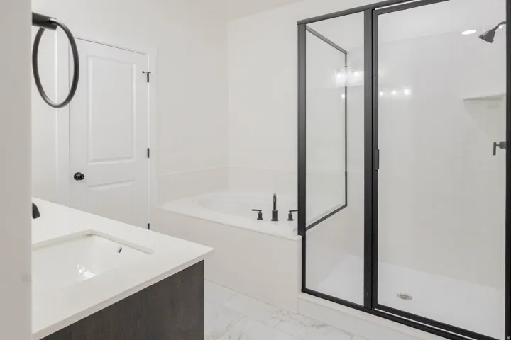 Modern bathroom featuring a built-in soaking tub with matte black fixtures, a walk-in shower with a black-framed glass enclosure, and a vanity with a white countertop and integrated sink
