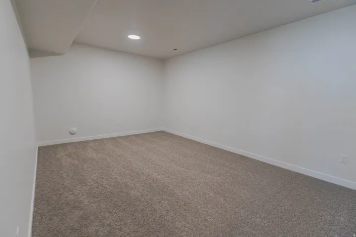 Spacious interior room featuring neutral-toned carpeting, white baseboards, and recessed ceiling lighting