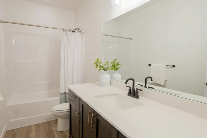 Contemporary bathroom featuring a dark wood-finish vanity with gold-tone hardware, a white countertop, an undermount sink, and a matte black faucet