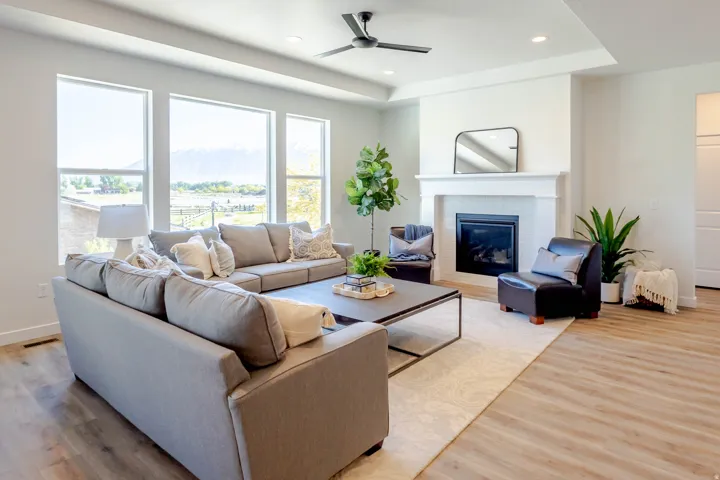 Spacious living area featuring large windows, wood-finish flooring, a contemporary ceiling fan, and a fireplace with a white mantel and tile surround