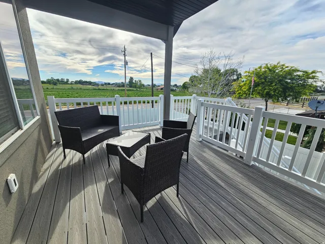 Spacious covered deck featuring composite wood-finish flooring, white railing, and a textured exterior wall