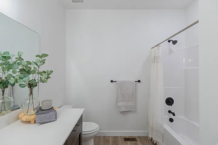 Bathroom featuring a white bathtub with a dark bronze shower fixture, a white countertop vanity with dark cabinetry, and wood-finish flooring