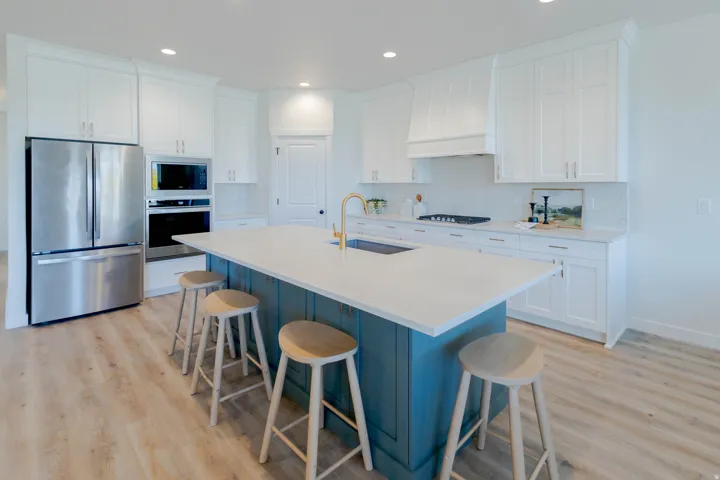 Contemporary kitchen featuring a large central island with a contrasting base, light-toned countertops, white shaker-style cabinetry, stainless steel appliances, and wood-finish flooring