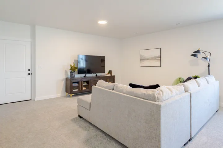 Spacious recreation room featuring light-toned carpet, recessed lighting, and a modern two-panel interior door with matte black hardware