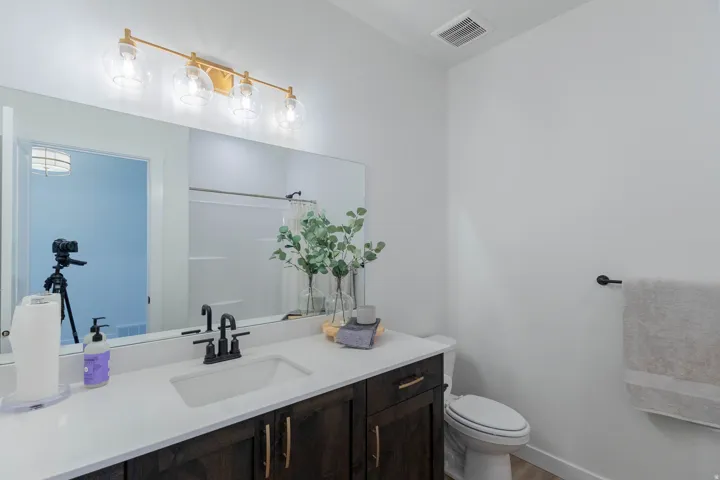 Modern bathroom featuring a dark wood-finish vanity with gold-tone hardware, white countertop, and integrated rectangular sink