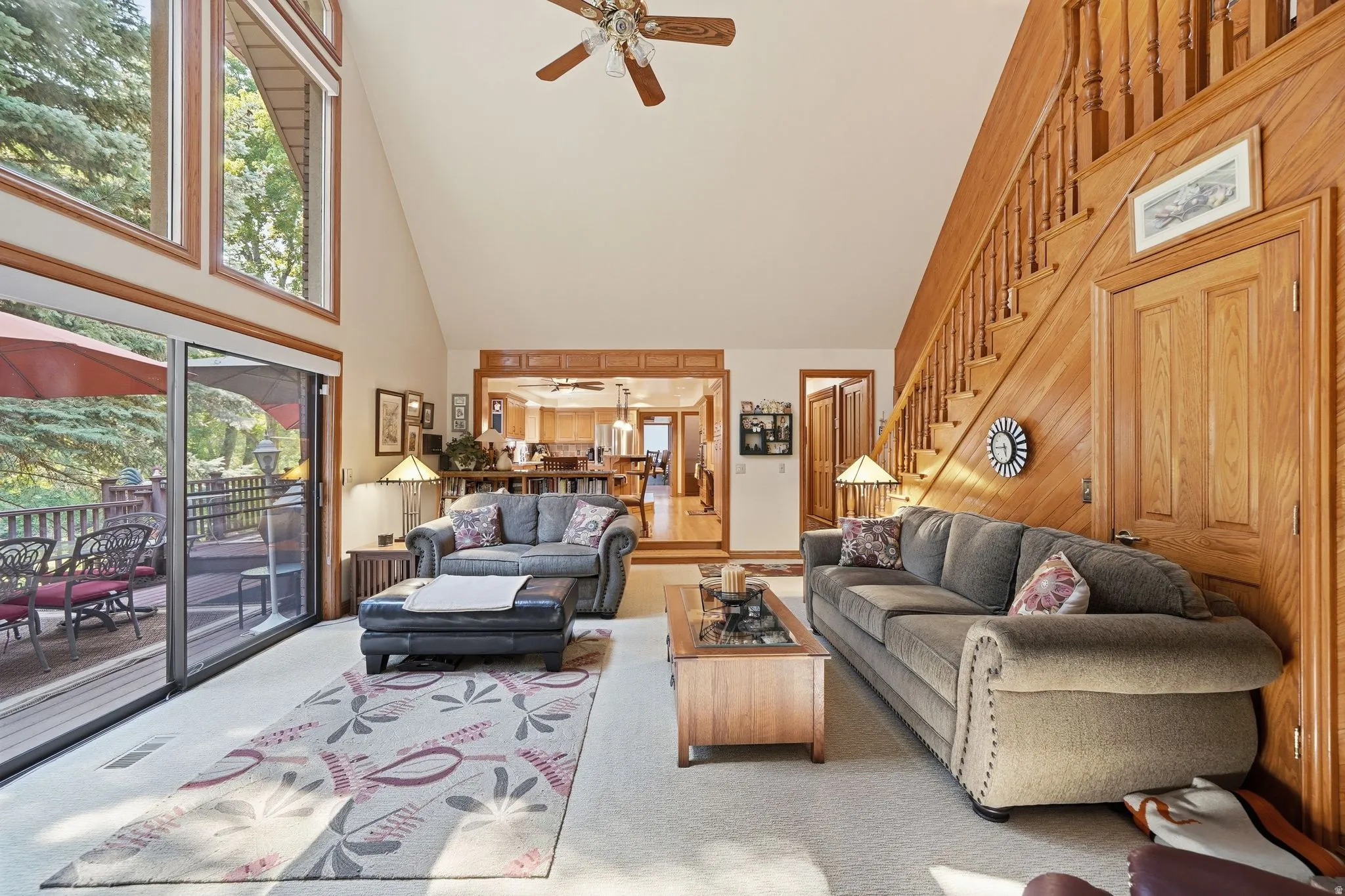 Vaulted living area featuring a wood-paneled accent wall, a solid wood staircase, and a ceiling fan