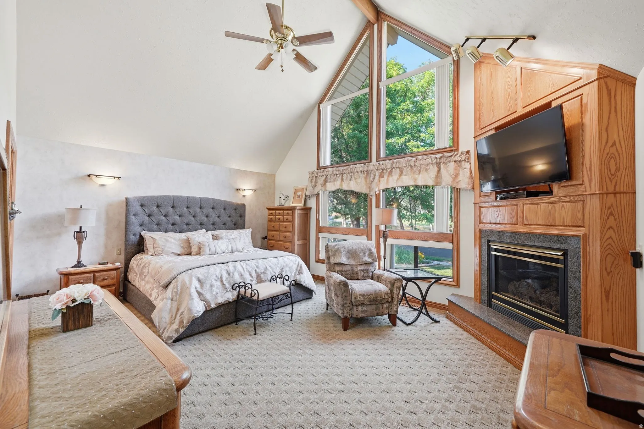 Vaulted ceiling interior featuring a ceiling fan, expansive windows with architectural angles, and a built-in entertainment center with a fireplace