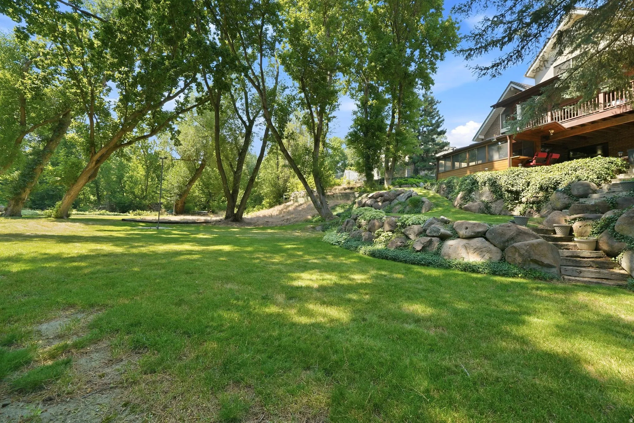 Expansive green lawn with mature trees and a multi-level rock retaining wall
