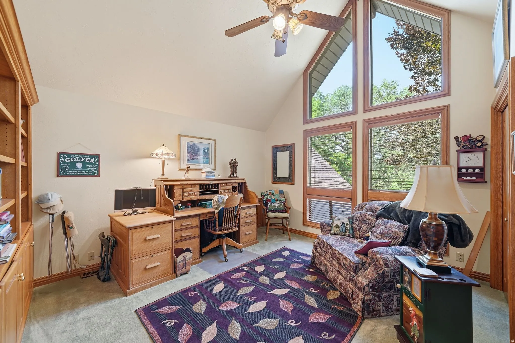 Vaulted ceiling room featuring extensive natural wood trim, a ceiling fan, and multiple large windows