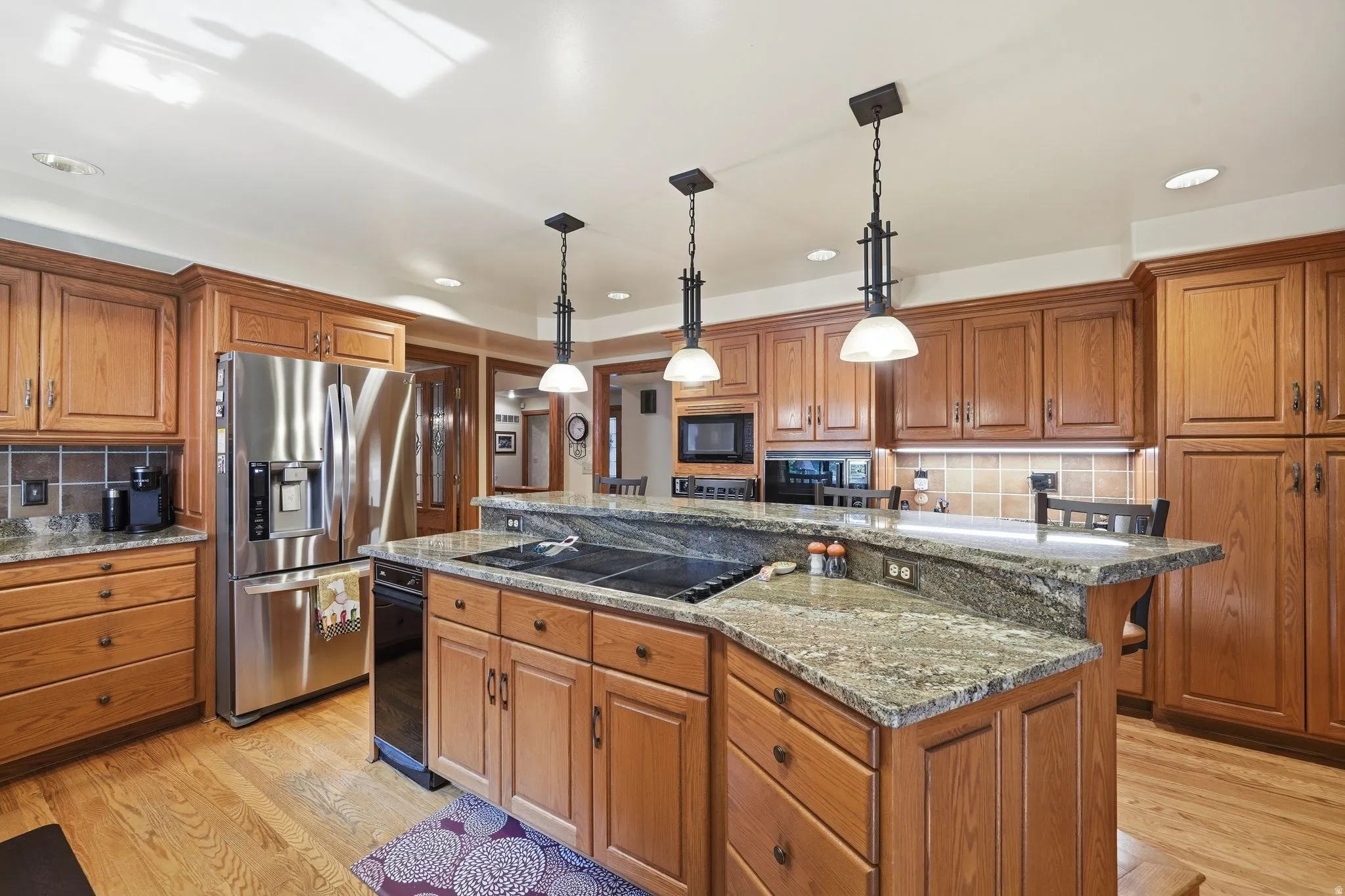 Spacious kitchen featuring warm wood cabinetry, granite countertops, and wood-finish flooring