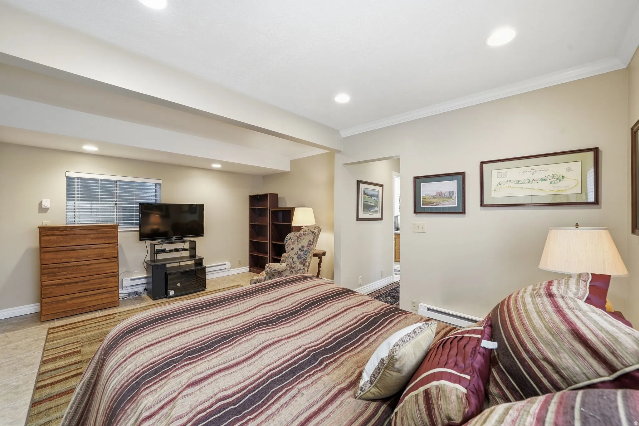 Recessed lighting illuminates this room, featuring light-colored walls, crown molding, and a window with blinds