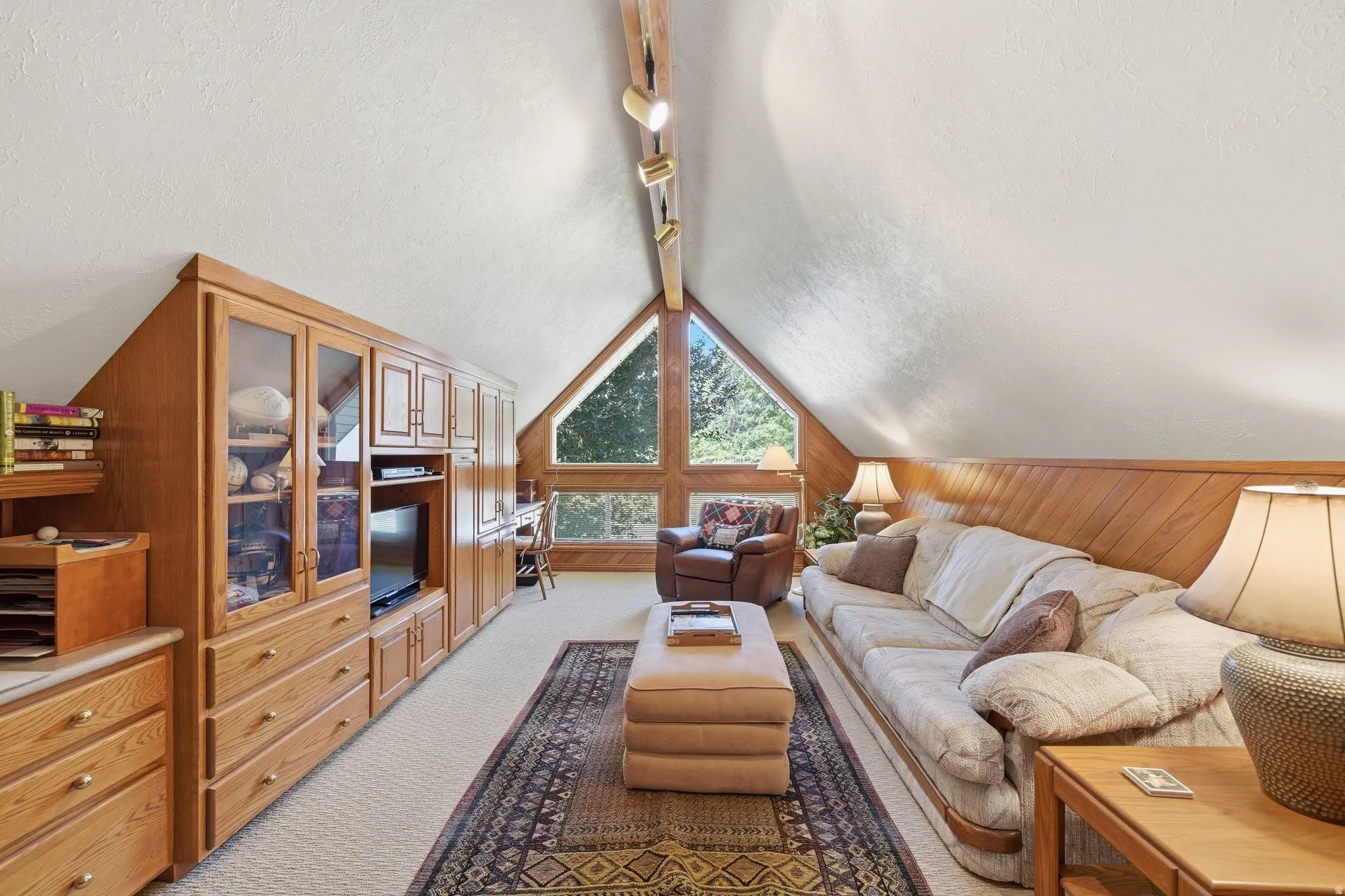 Angled ceiling room featuring built-in wood cabinetry, wood-paneled walls, and a large triangular window