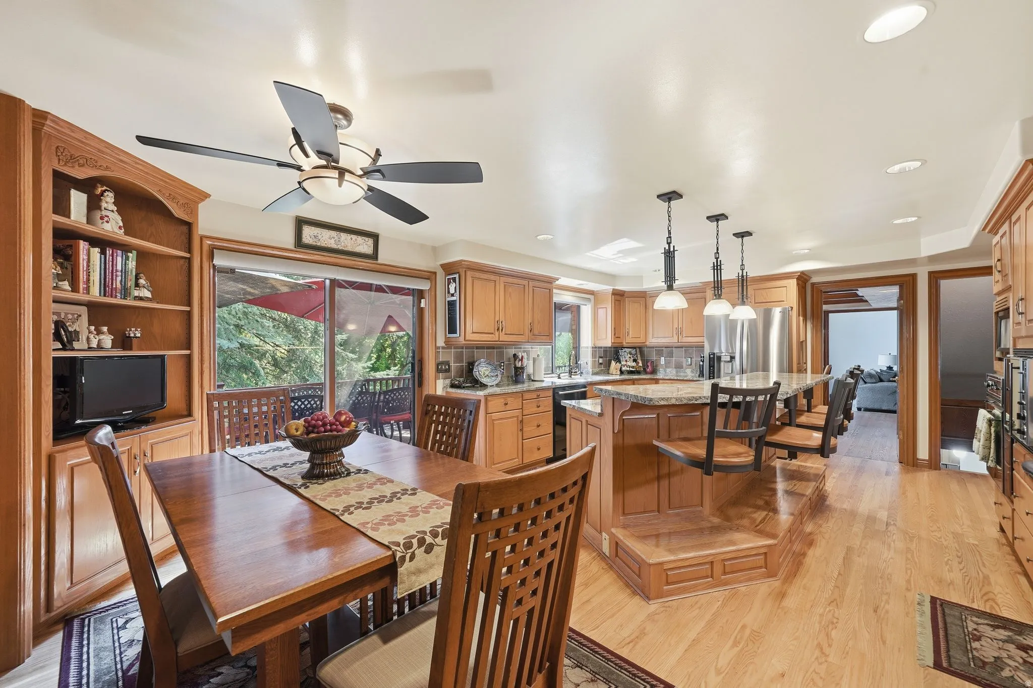 Open-concept kitchen and dining area featuring wood-finish flooring, custom built-in cabinetry, granite-style countertops, stainless steel appliances, and a central island with integrated seating