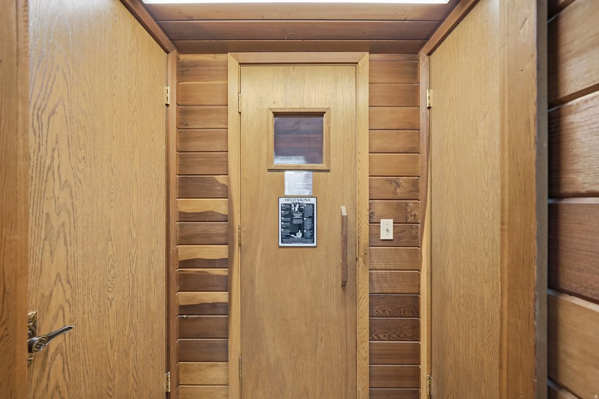 Wood-paneled room featuring a central wood door with a small window, flanked by two additional wood doors