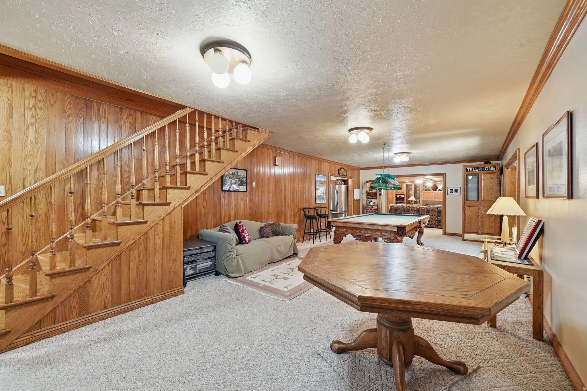 Spacious recreation area featuring wood paneling throughout, a prominent wooden staircase, and recessed lighting