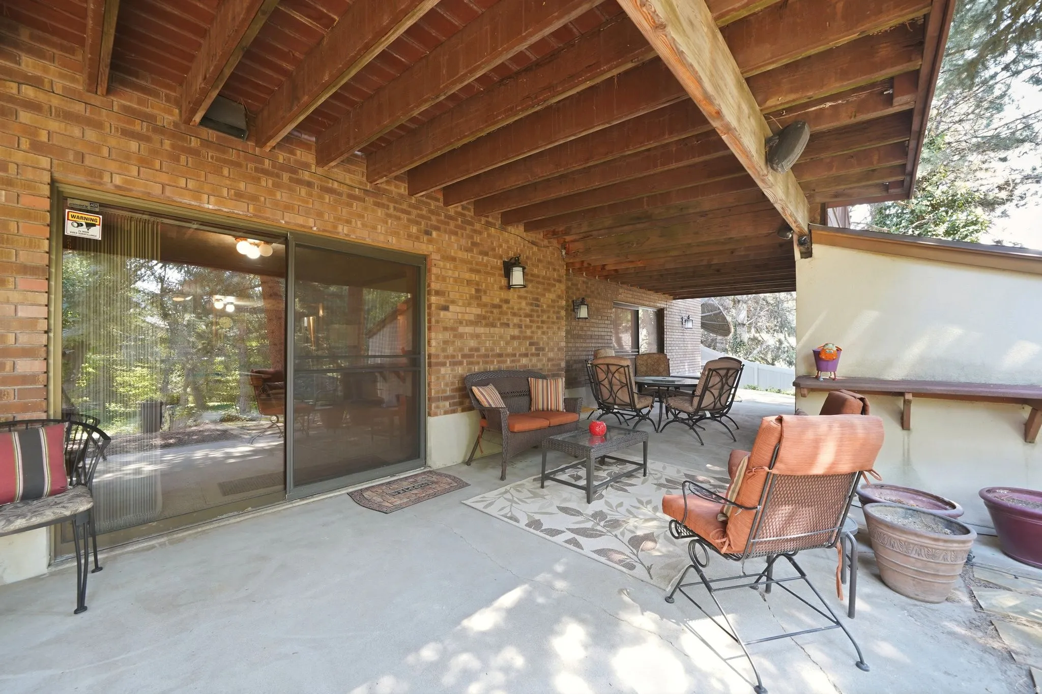 Covered outdoor patio featuring a concrete surface, exposed wood beam ceiling, and a brick exterior wall