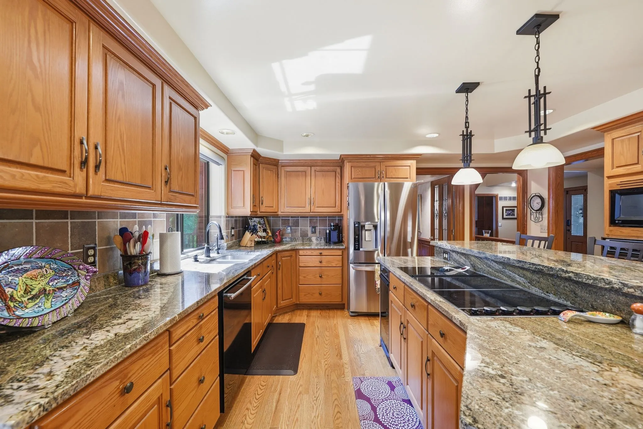Kitchen featuring wood cabinetry, light-colored countertops, stainless steel refrigerator, built-in cooktop, and hardwood flooring