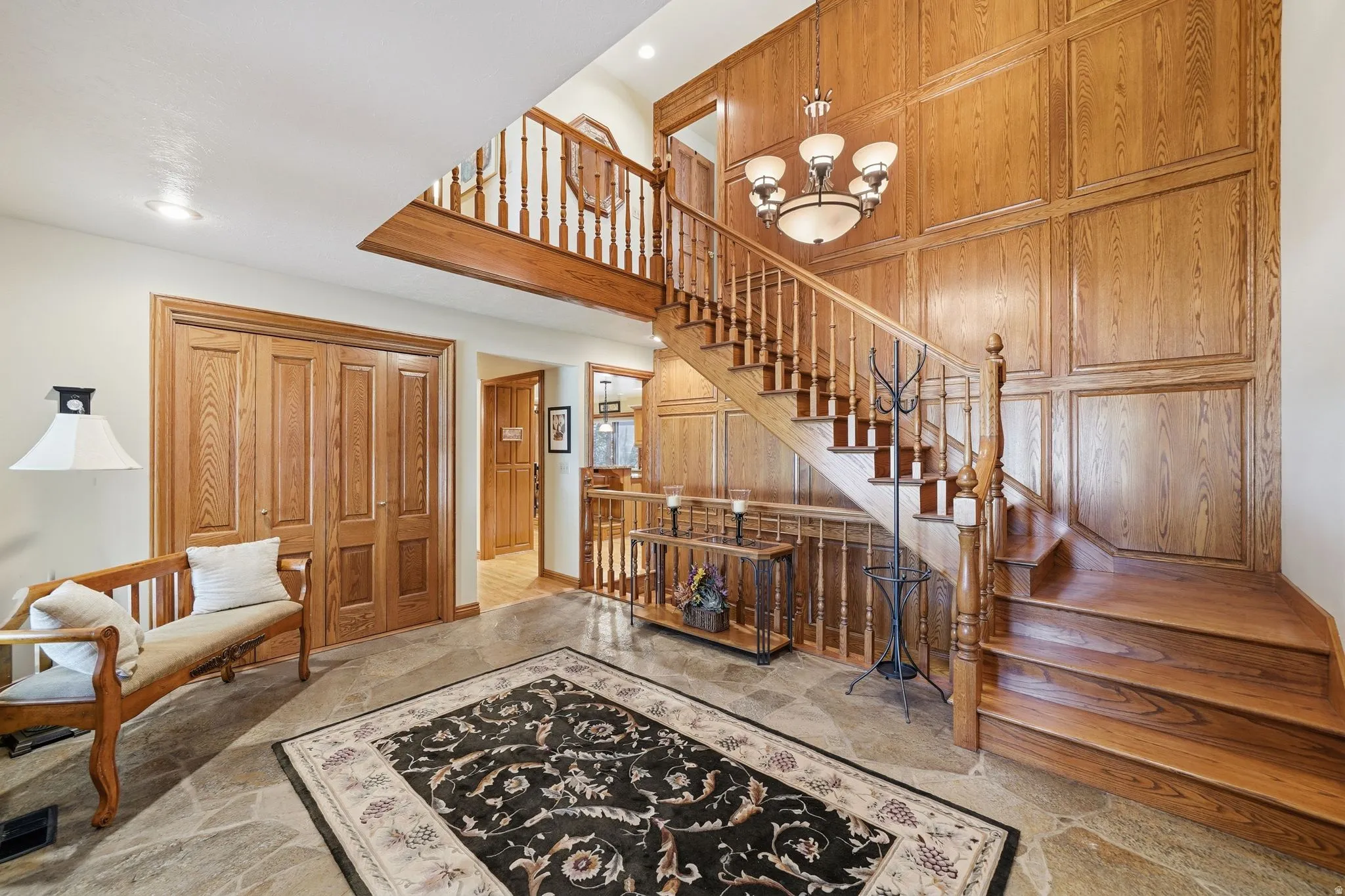 Grand foyer featuring a natural stone floor, a prominent wood staircase with wrought iron balusters, and extensive wood paneling