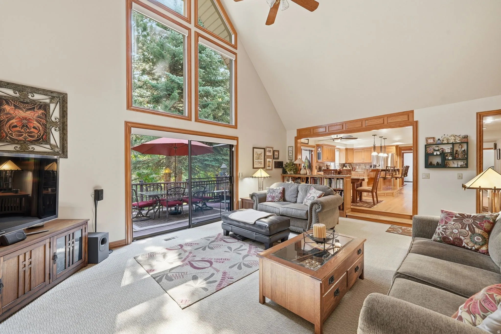 Vaulted living area featuring high ceilings, a wall of wood-framed windows, carpet flooring, and direct access to an outdoor deck